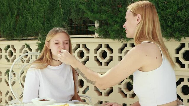 Mom lovingly feeds her teenage daughter delicious churos outdoors, enjoying  warm day and pleasant conversation.