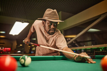 Dramatic portrait of adult African American man playing pool and hitting ball with cue stick in pool club copy space - 782449686