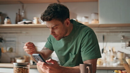 Domestic businessman watching smartphone at morning kitchen closeup. Man eating