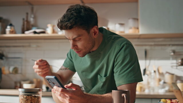 Domestic businessman watching smartphone at morning kitchen closeup. Man eating - Powered by Adobe