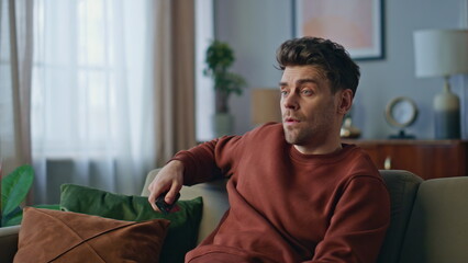 Dissatisfied guy watching television at couch close up. Bored brunet switching