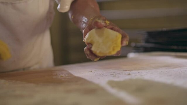 Man shapes portions of dough with his hands on a wooden table, adding flour for integration.