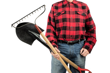 A landscape worker  in a red and black lumberjack shirt holds a round nose shovel and a garden rake...