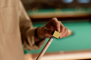 Close up of unrecognizable man using chalk cube on cue stick while playing pool copy space