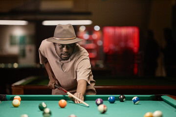 Waist up portrait of adult African American man wearing hat and hitting ball with cue stick while playing pool copy space - 782458490
