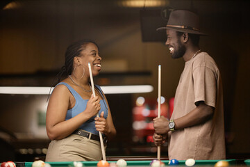 Side view portrait of smiling African American couple chatting by pool table in nightclub - 782459062