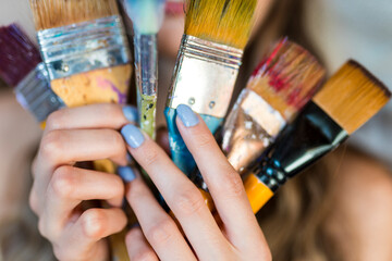 Close up portrait of beautiful female artist with different paints on them, holding paint brushes...