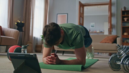 Athlete following online lesson standing plank position on yoga mat home.