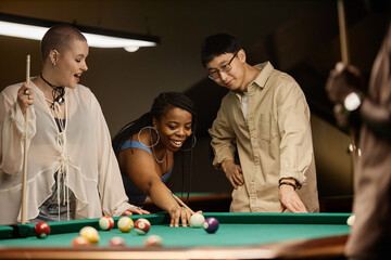 Portrait of diverse group of friends with African American woman playing pool in nightclub in muted tones