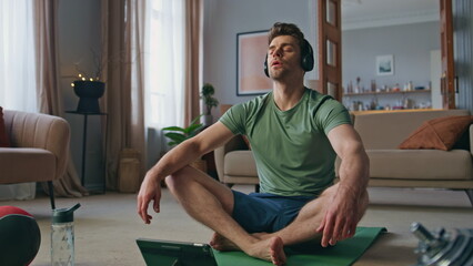 Relaxed guy sitting lotus position in headphones at home. Closed eyes yoga man