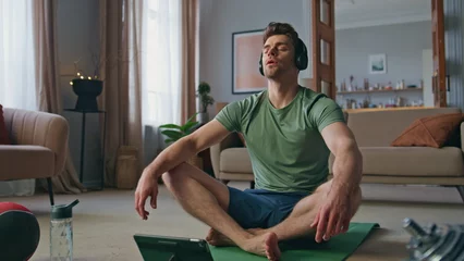 Fotobehang Relaxed guy sitting lotus position in headphones at home. Closed eyes yoga man © stockbusters