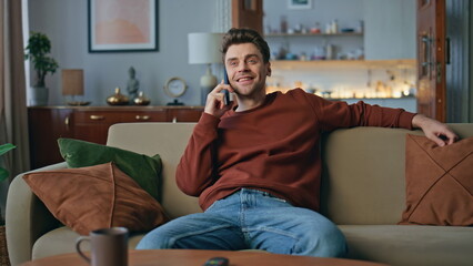 Resting guy communicating smartphone at cozy couch. Happy man talking cellphone