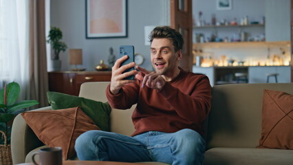 Happy blogger streaming smartphone in modern living room. Cheerful man laughing