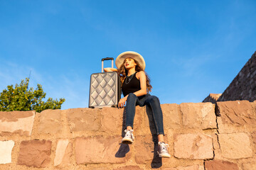 young woman in straw hat with suitcase in city. Portrait of a happy female tourist on a summer journey. 