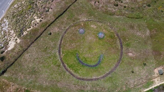 Drone rising from Happy Face art on a hill by 118 highway Simi Valley