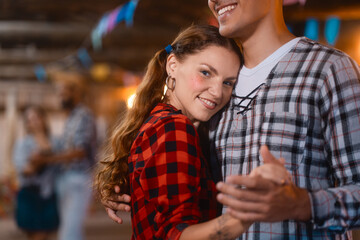 Affectionate young woman in checkered attire dancing closely with her partner at a Festa Junina....