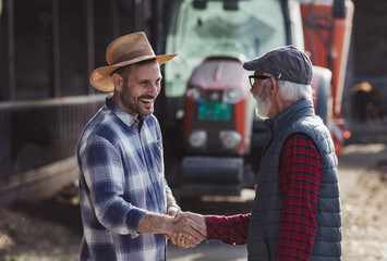 Farmers shaking hands in front of tractor on cattle farm