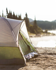 Green camping tent in the morning light with lake, mountains and trees in the background