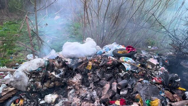 Environmental disaster: plastic waste and toxic garbage burning on a landfill site. Thick smoke and fire flames from burning trash dump. Air pollution, ecological crisis and climate change concept.