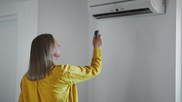 Woman holding remote control aimed at the air conditioner.
