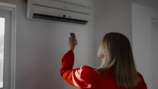 Woman in red dress holding remote control aimed at the air conditioner.