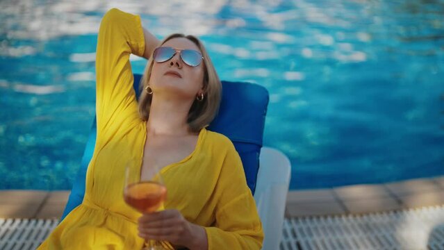 Pretty woman with wine relaxing by the pool.