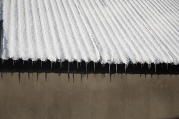 Roof covered in snow. Icicles on the roof visor. Frozen building.