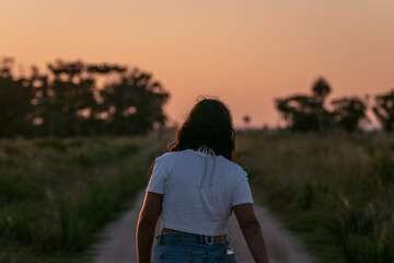 Woman walking on a dirt road at sunset