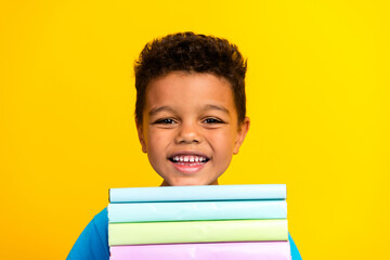 Photo of funny cute child with curly hair dressed blue stylish t-shirt holding book learn lessons isolated on vibrant yellow background