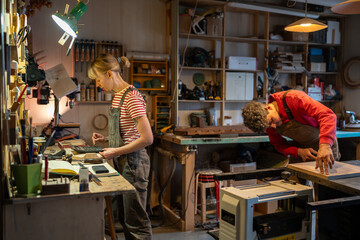 Family carpentry workshop, young couple of carpenters working on wood in studio with wooden items,...