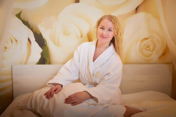 A blonde girl in a white terry bathrobe in a hotel room after spa treatments on a trip or travel. Weekend and vacation body care