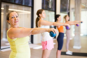 Women holding dumbbells in each hand and doing exercises in fitness room