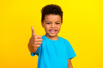 Photo of mixed race satisfied child with curly hair dressed blue t-shirt showing thumb up approve...