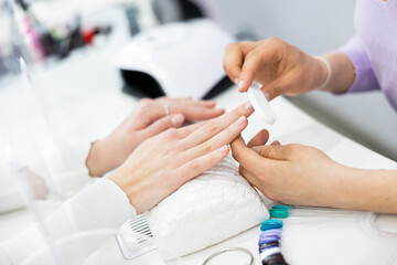 Woman manicurist filing and shaping nails of female client during procedure of manicure in beauty...