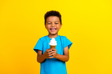 Photo of satisfied cheerful child with curly hair dressed blue t-shirt holding tasty ice cream...