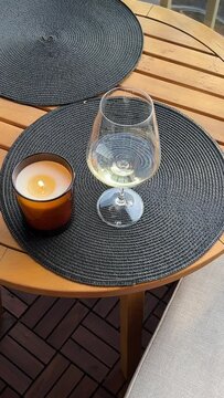 Female hand putting burning candle on the table near the glass of white wine