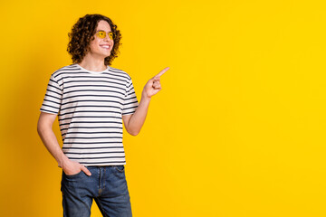 Photo of nice young man point finger empty space wear striped t-shirt isolated on yellow color...