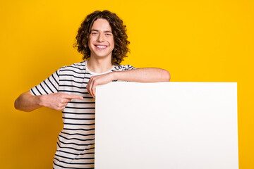 Photo of nice young man point finger empty space blank wear striped t-shirt isolated on yellow color background