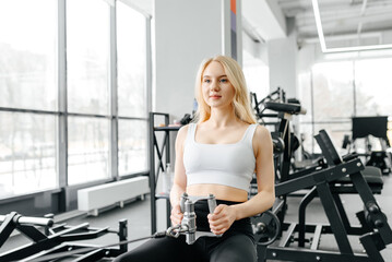 young athletic caucasian woman trains in fitness gym, thrust in block simulator, blonde girl in white top and black leggings, healthy lifestyle concept