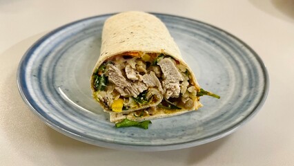 small fried pieces of chicken meat with vegetables, corn wrapped in pita bread on a gray plate on a white table and side view. Healthy snack healthy food