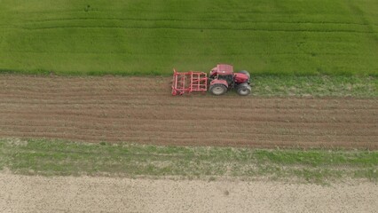 Aerial view of red tractor with seeder plows and plants grain seeds in ground of agricultural field...