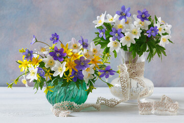Two bouquets of spring blue, purple, white and yellow flowers in vases on the table, a beautiful still life. - 782516676