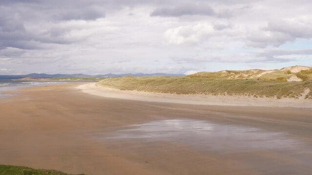 Sand dunes, panning left to show a golden beach on an overcast day. Tullan Strand, Co. Donegal, Ireland.