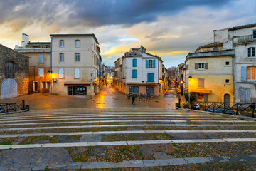 Illuminated shops and cafes after an evening rain seen from the steps of the ancient arena in the historic medieval old town of Arles, France, in the Provence region.