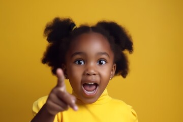 Joyful young girl pointing, mix race girl, vibrant yellow background, excited expression - obrazy, fototapety, plakaty
