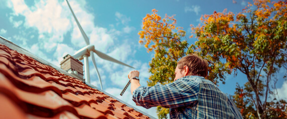 A man reaching towards a wind turbine on a rooftop with solar panels, representing hands-on renewable energy implementation in urban settings. Caring for the environment. Banner. Copy space