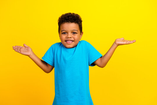 Photo of funky clueless child with curly hair dressed blue t-shirt shrug shoulders have no idea isolated on vibrant yellow background