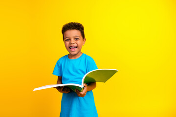 Photo of cheerful small child with curly hair dressed blue stylish t-shirt holding book having fun...