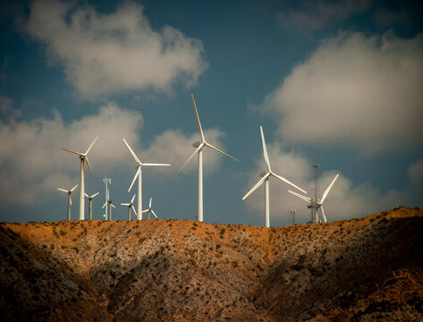 A group of large white wind turbines in the desert against a blue sky with clouds. The image was made near Palm Springs California