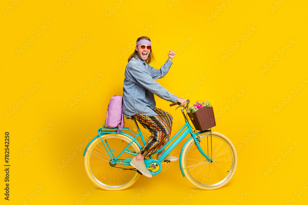 Sticker Full body portrait of cool young man ride bike raise fist wear denim shirt isolated on yellow color background